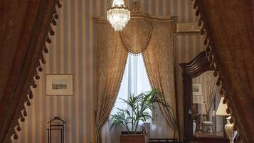 A bedroom with a large bed, a chair, a desk, a mirror, and a chandelier.