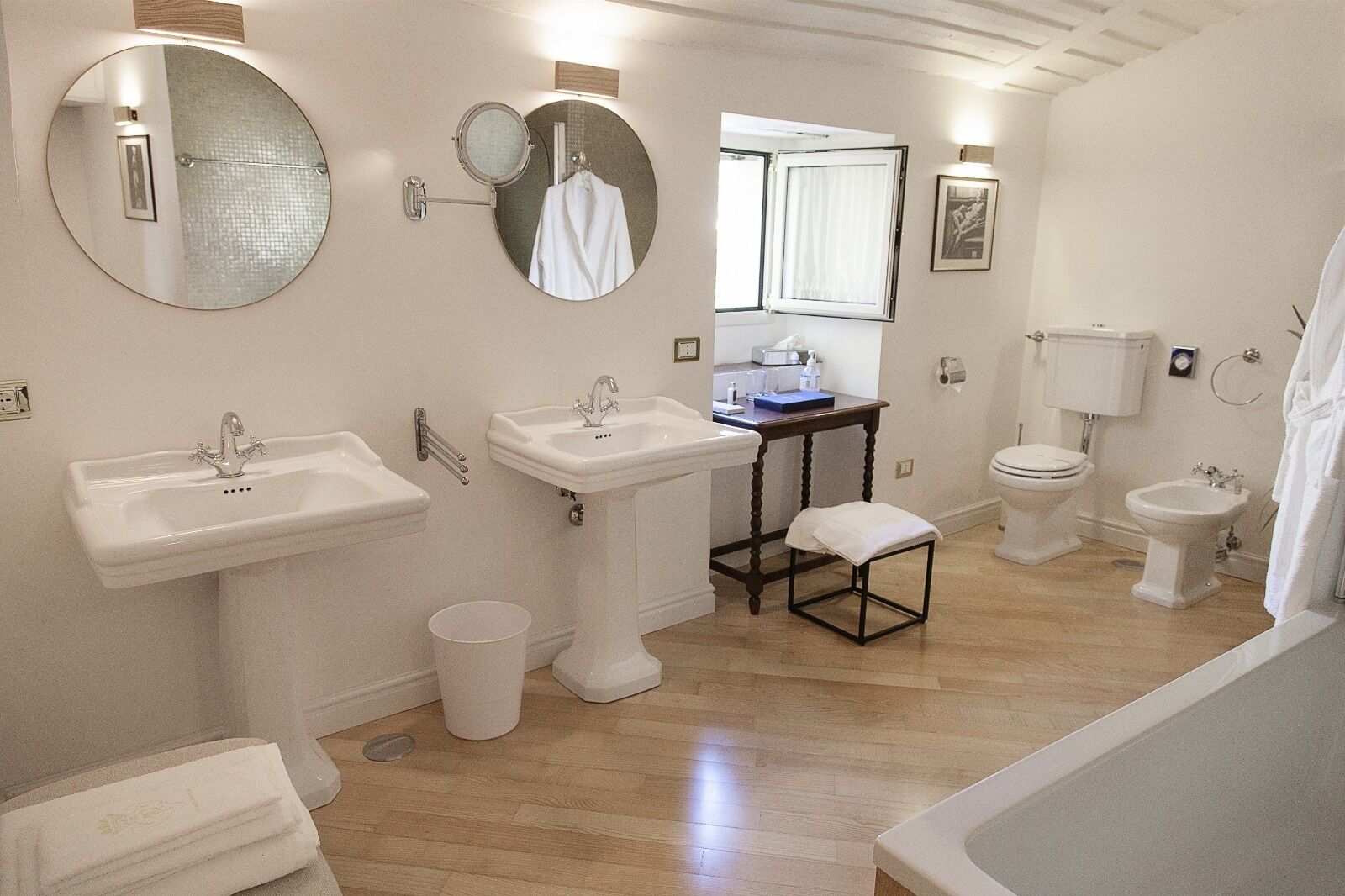 A bathroom with a sink, two toilets, a bidet, a mirror, and a small table with a towel.