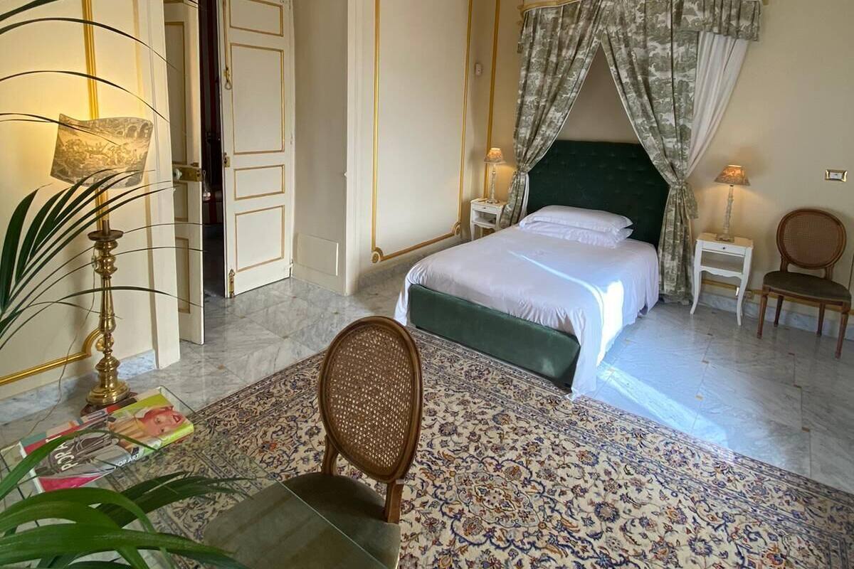 Ein geräumiges Schlafzimmer mit einem großen Bett, einer Chandelüster, einem grünen Kopfteil und einem gemusterten Teppich.