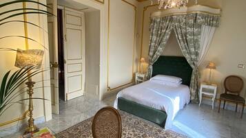 A spacious bedroom with a large bed, a chandelier, a green headboard, and a patterned carpet.