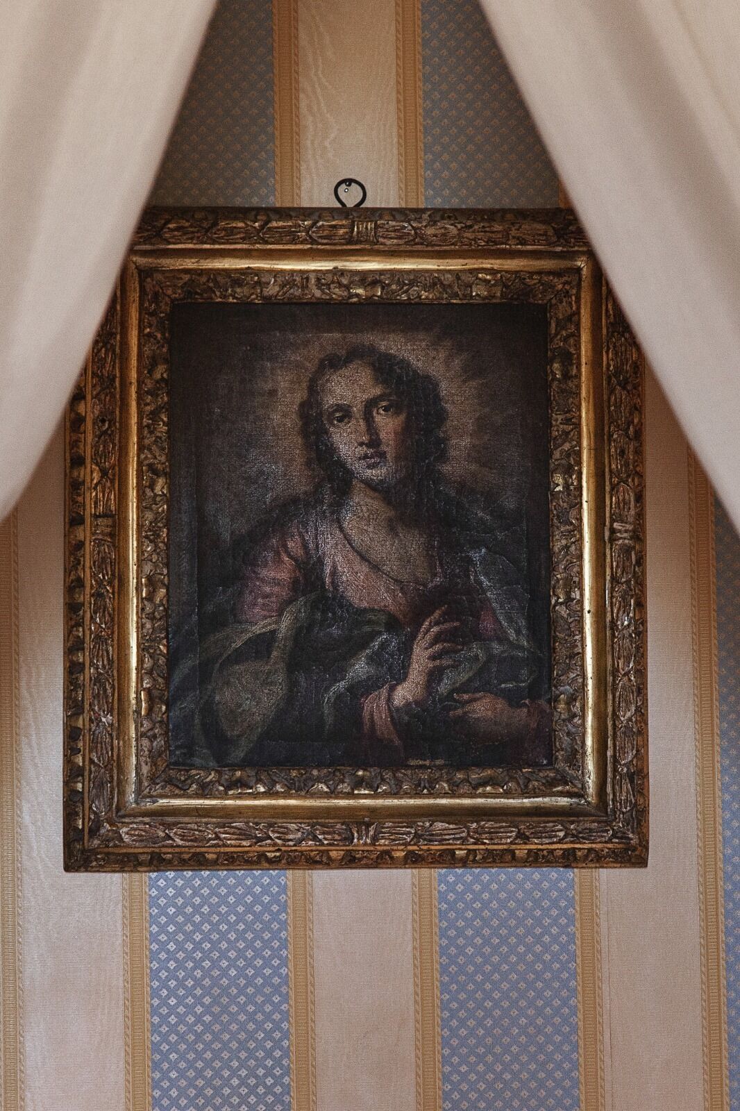Ein gerahmtes Kunstwerk mit dunklem, strukturiertem Hintergrund und einer Person in einer Robe, an einer Wand mit Streifenmuster befestigt.