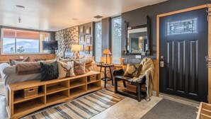 Un salon chaleureux avec un mur en pierre, une porte noire et une grande fenêtre donnant sur un paysage enneigé.
