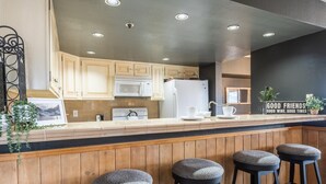 Une cuisine moderne avec des meubles en bois, un réfrigérateur blanc et un coin bar équipé de tabourets.