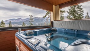 Un bain à remous avec un revêtement extérieur en bois et une vue sur les montagnes et les arbres.