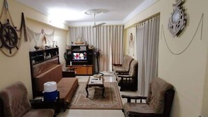 Ein Wohnzimmer mit einer Couch, Sesseln, einem Couchtisch, einem Fernseher und einer Wandverzierungen.