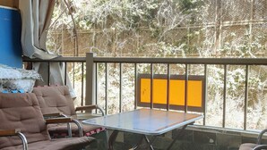 Ein Balkon mit Tisch und Stühlen, einer grünen Matte und Blick auf Grünflächen und ein Gebäude.