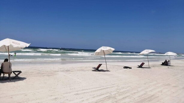 Ein Strand mit weißen Sonnenschirmen und Liegen, einem klaren Himmel und dem Meer im Hintergrund.