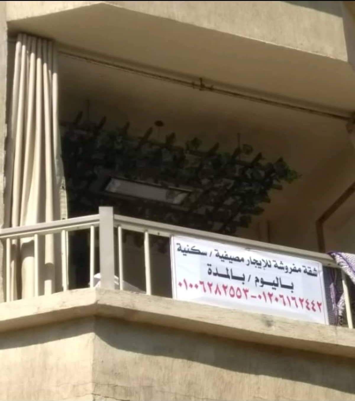 A building with a balcony, a sign with Arabic text, and a plant.