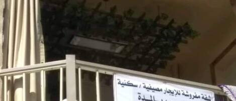 A building with a balcony, a sign with Arabic text, and a plant.