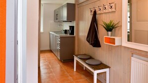 A hallway with a bench, a coat rack, a potted plant, and a door leading to a kitchen.