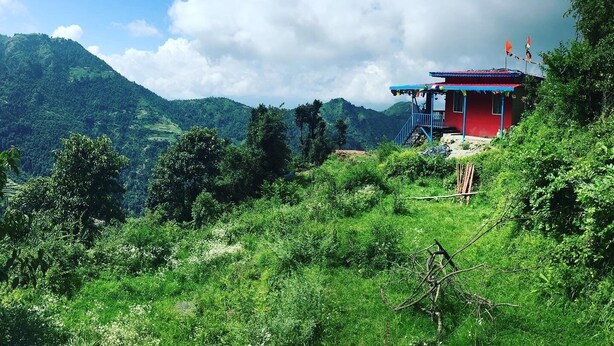 A red building with a blue roof, surrounded by lush greenery and hills in the background. - Mountains, jungle , Trekking and luxury stay near to nature (Dhanolti)