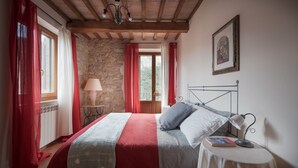 A bedroom with a bed, a bedside table, a lamp, a framed picture on the wall, and a window with curtains. - Folaga Apartments, "Puntone" (Sant'Arcangelo)