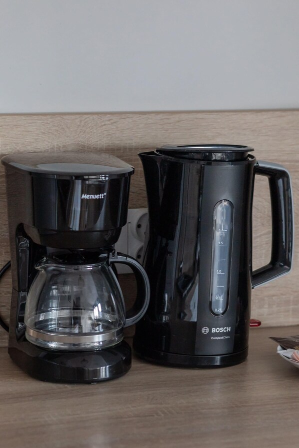 A black coffee maker and a black electric kettle on a wooden surface.