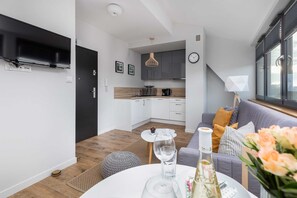 Ein modernes Wohnzimmer mit einer Couch, einem Esstisch mit einem Weinglas und einer Küche im Hintergrund.