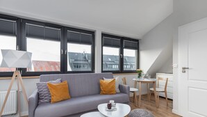 A modern living room with a grey sofa, white coffee table, and a dining area with a small table and chairs. - Comfortable Studio | Parking, SPA, Close to the Beach (Kołobrzeg)