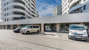 A modern building with a curved facade, a covered parking area, and two white vans parked in front.