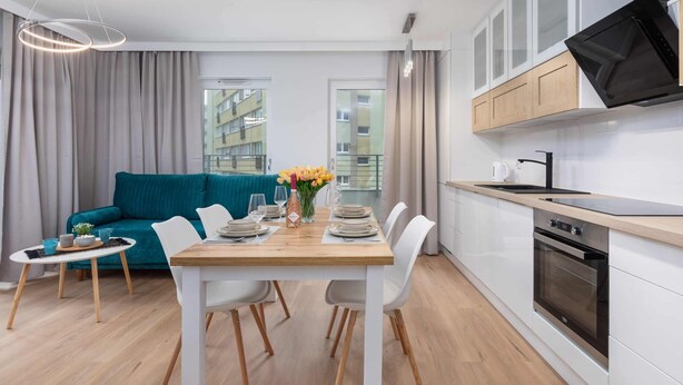 A modern kitchen with white cabinets, a built-in oven, and a flat-screen TV.