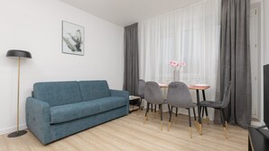 Una sala de estar moderna con un sofá azul, una mesa de comedor con sillas, una lámpara de pie y un cuadro en la pared.