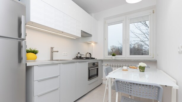 Una cocina moderna con armarios blancos, un refrigerador de acero inoxidable, una estufa a gas y una ventana con vista a árboles.