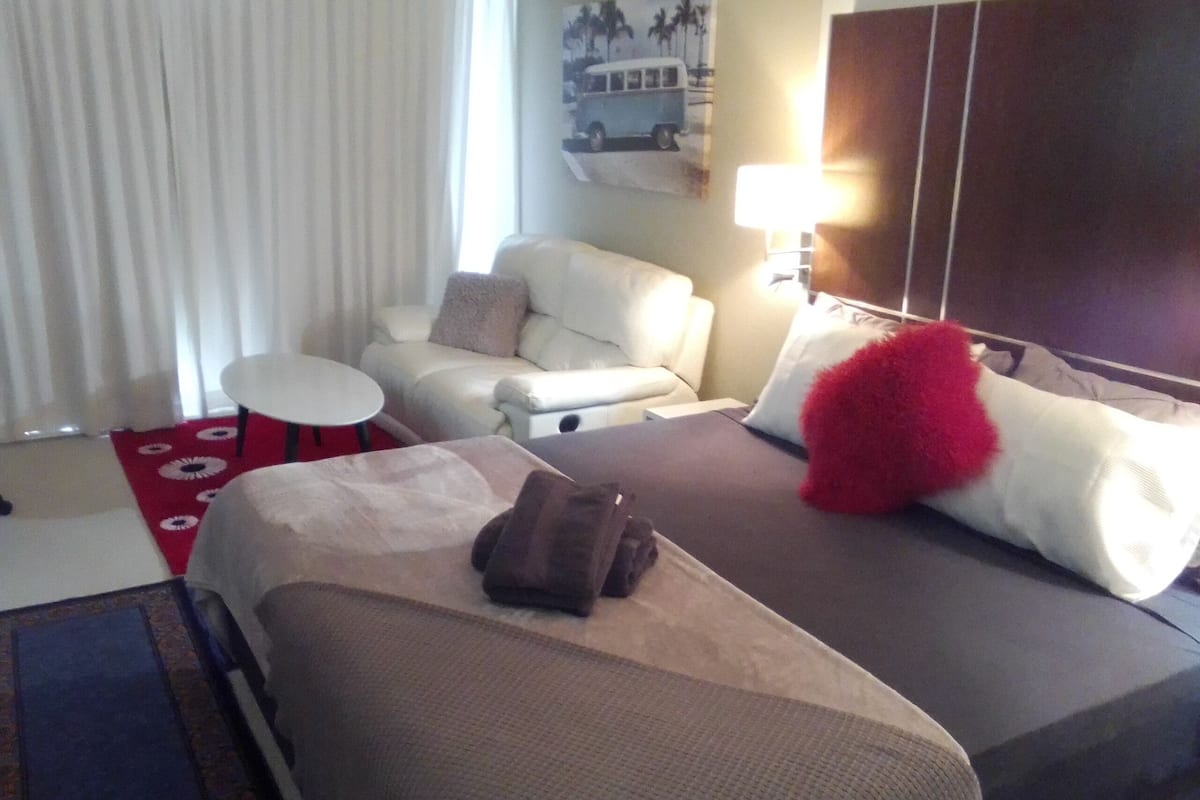 A hotel room with a bed, a small table, a sofa, and a lamp.