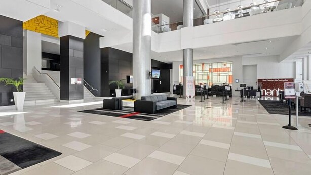A spacious lobby with a modern design, featuring a central seating area, a staircase, and a large window providing natural light. - Your Stay In Surfers (Surfers Paradise)