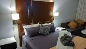 A hotel room with a large bed, a nightstand, a desk, and a chair. - Your Stay In Surfers (Surfers Paradise)