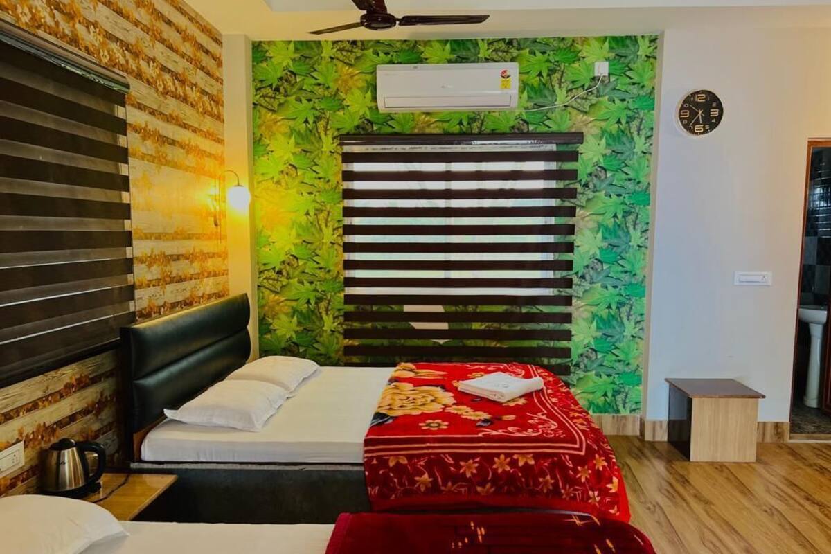 A hotel room with a bed, a red upholstered bench, a wall-mounted air conditioner, and a ceiling fan.