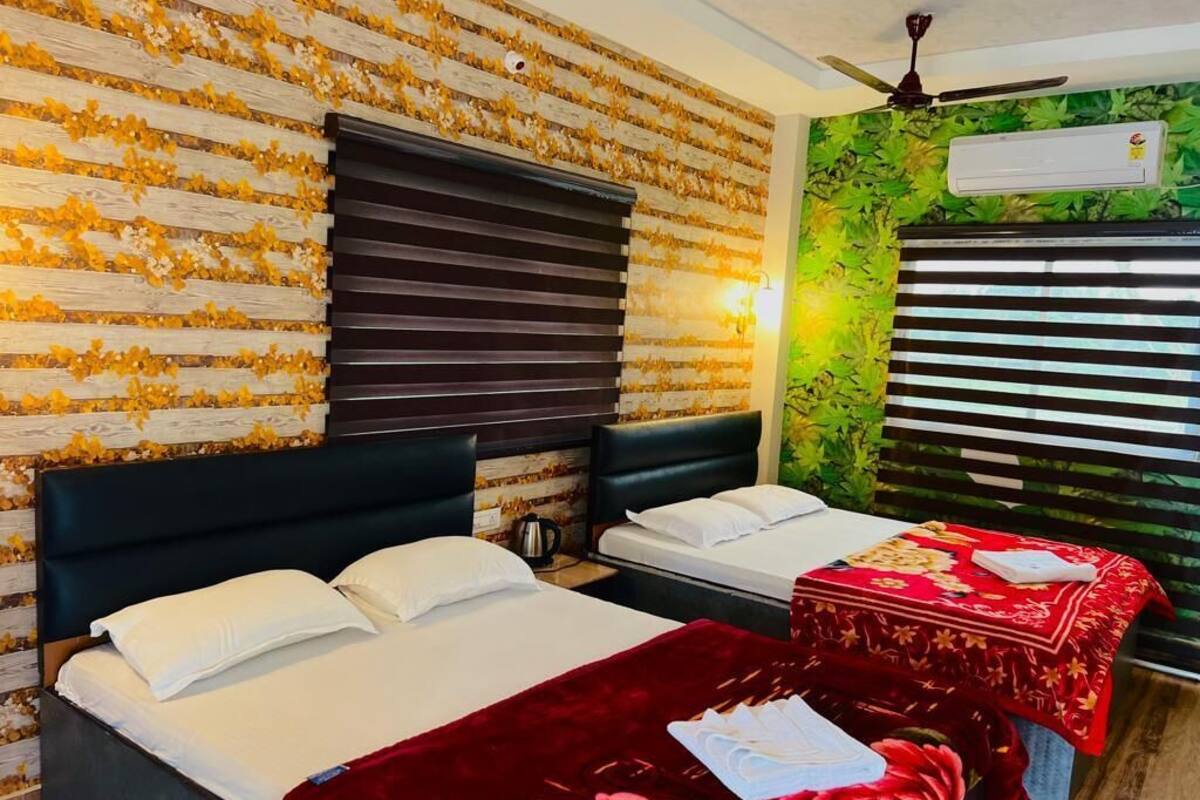 A hotel room with two beds, a red floral bedspread, a wooden wall with yellow flowers, and an air conditioning unit.
