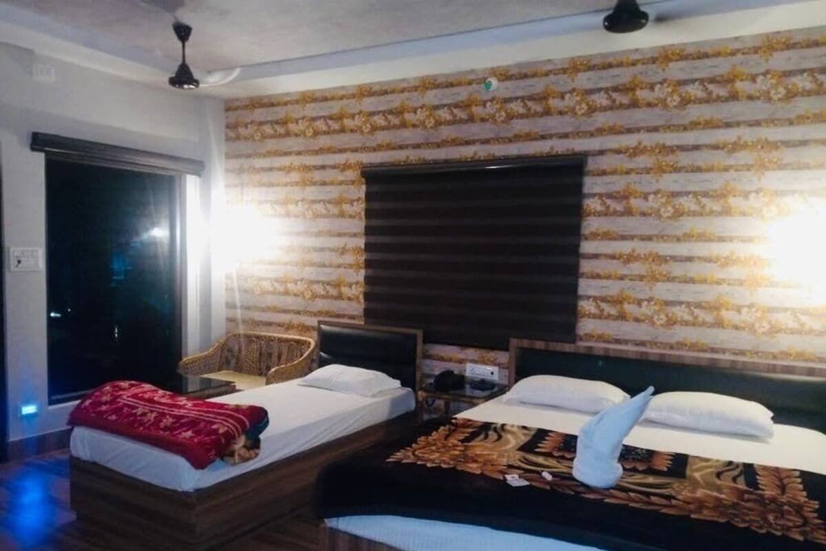 A hotel room with two beds, a sofa, a wooden floor, a patterned wall, and a window with blinds.