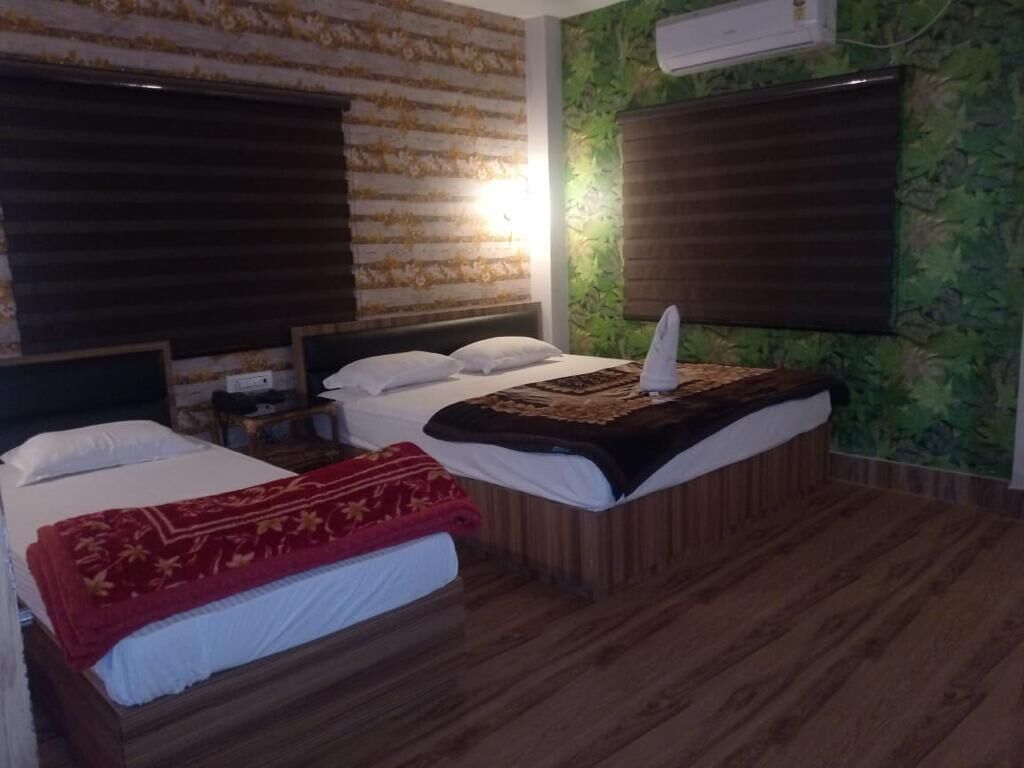A hotel room with two beds, wooden flooring, and a green wall with a leaf pattern.