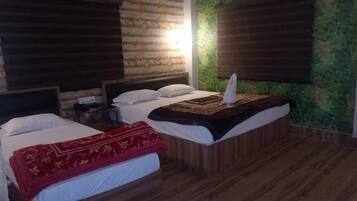 A hotel room with two beds, wooden flooring, and a green wall with a leaf pattern.