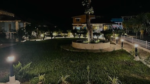 Vista nocturna de un patio con un jardín circular en el centro, rodeado de edificios con ventanas iluminadas.