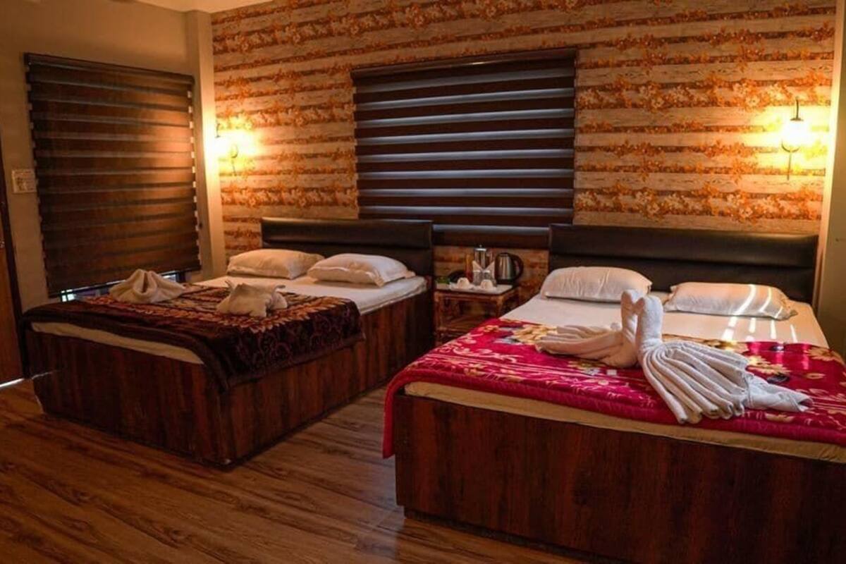 A hotel room with two wooden beds, a brick-patterned wall, and two wall-mounted lamps.