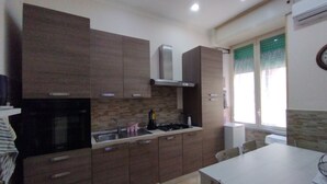 A modern kitchen with dark wooden cabinets, a stainless steel sink, and a small dining table. - The window in front of Naples (Napoli)