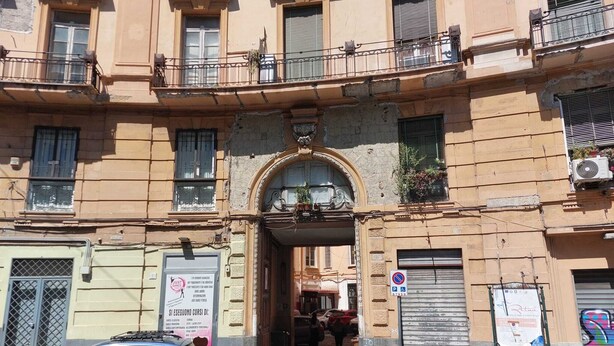 A building entrance with a sign for dance lessons, a parking sign, and two parked cars. - The window in front of Naples (Napoli)