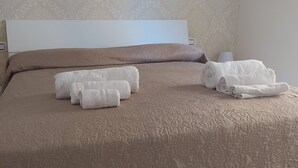A neatly made bed with a brown textured bedspread and two rolled white towels. - The window in front of Naples (Napoli)