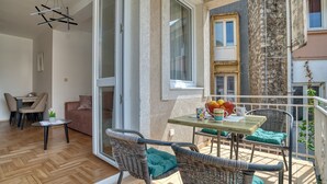 Ein Balkon mit Korbstühlen und einem Tisch, ein Essbereich mit Stühlen und einem Tisch sowie eine Glastür zum Innenraum.