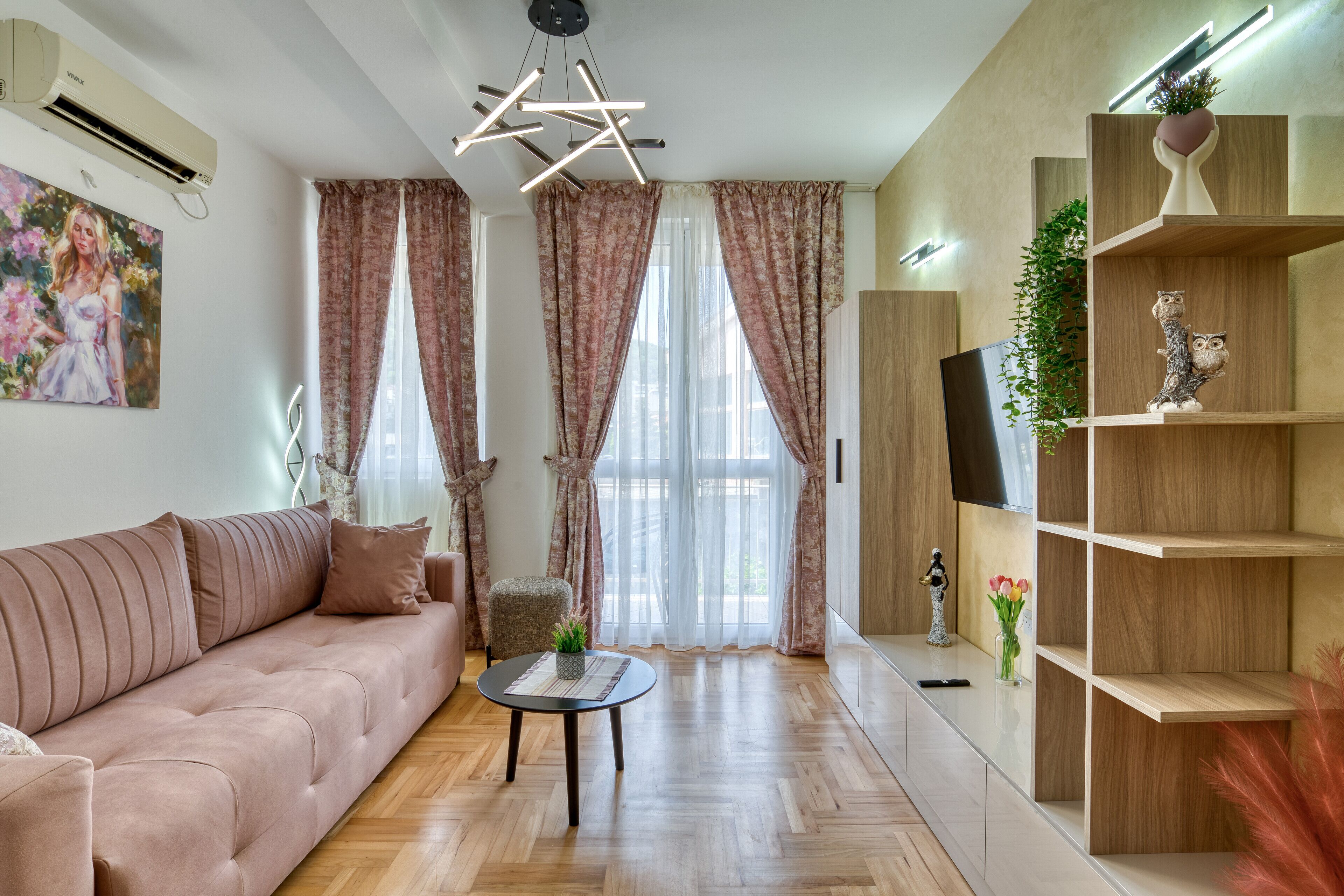 A modern living room with a sofa, a small round table, and a TV on a wooden shelf.