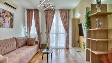 A modern living room with a sofa, a small round table, and a TV on a wooden shelf.