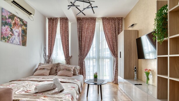 Ein modernes Schlafzimmer mit Bett, Nachttisch, Fernseher und einer Pflanze.