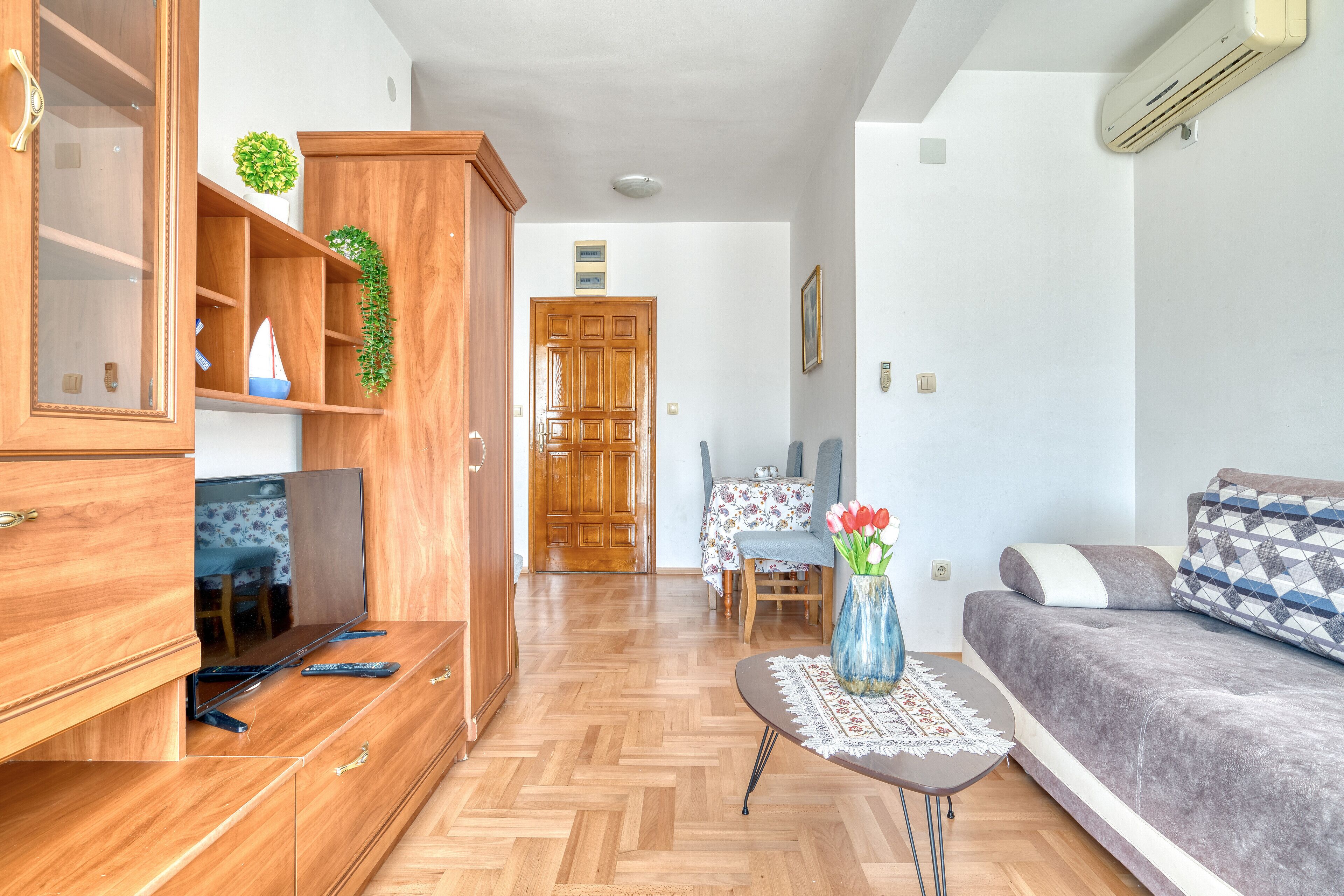 Una sala de estar con sofá, televisión, armarios de madera y un comedor con mesa y sillas.