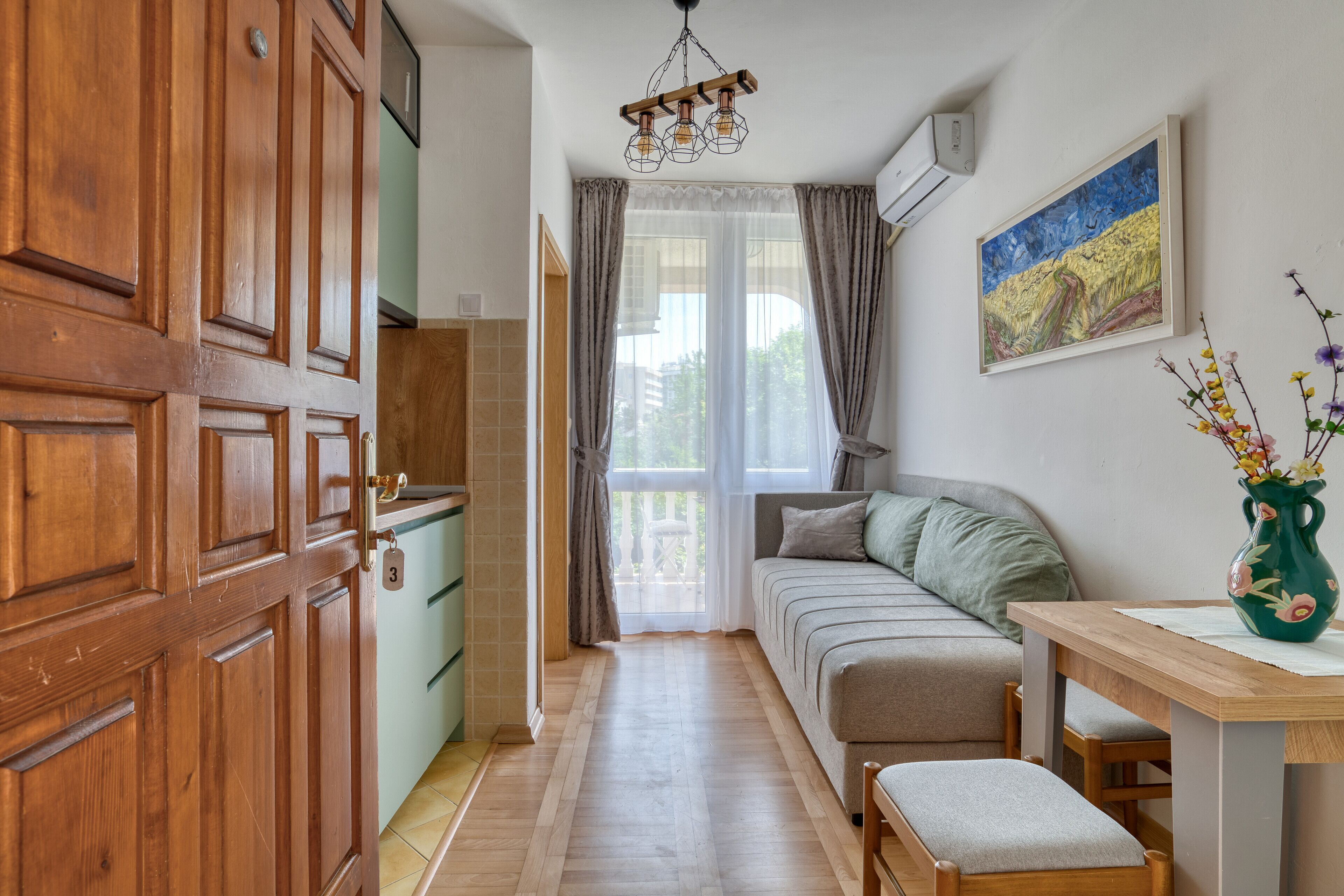 A narrow hallway with a wooden door, a green sofa, a wooden table, and a painting on the wall.