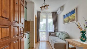 A narrow hallway with a wooden door, a green sofa, a wooden table, and a painting on the wall.