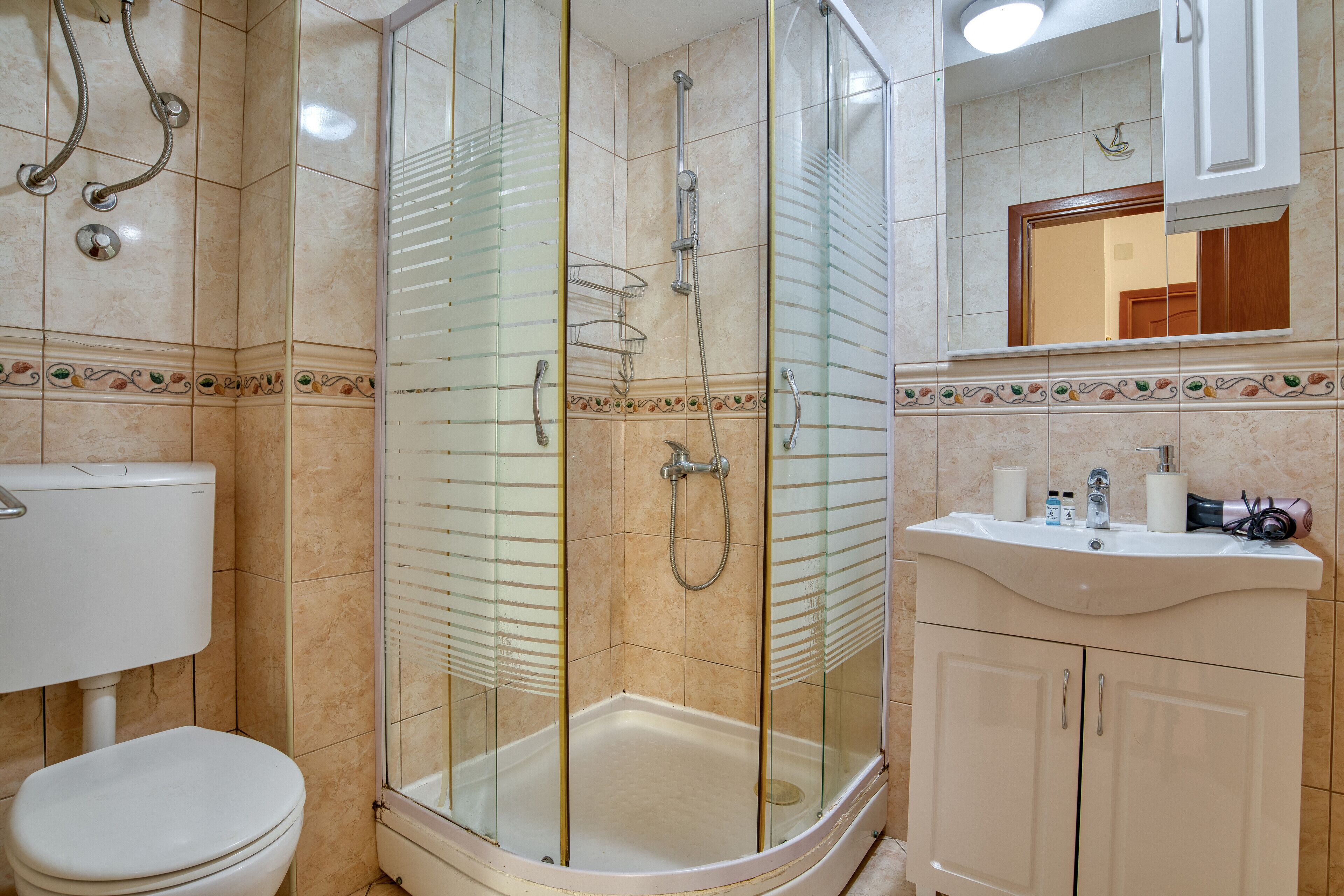 Un baño con ducha envuelta en vidrio, inodoro y lavamanos con artículos de tocador.