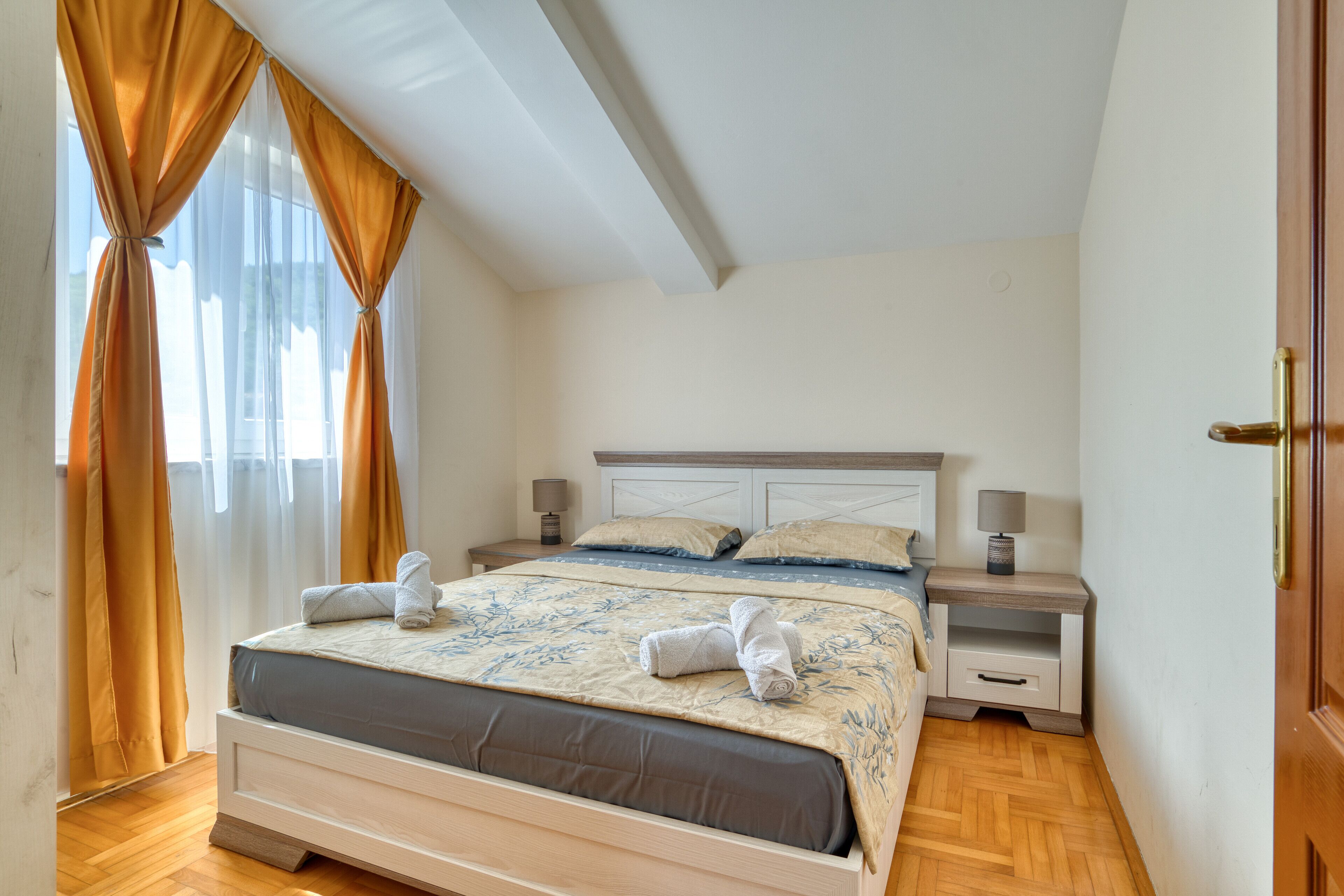 A neatly made bed with a blue and white patterned bedspread, two bedside tables with lamps, and a window with curtains.
