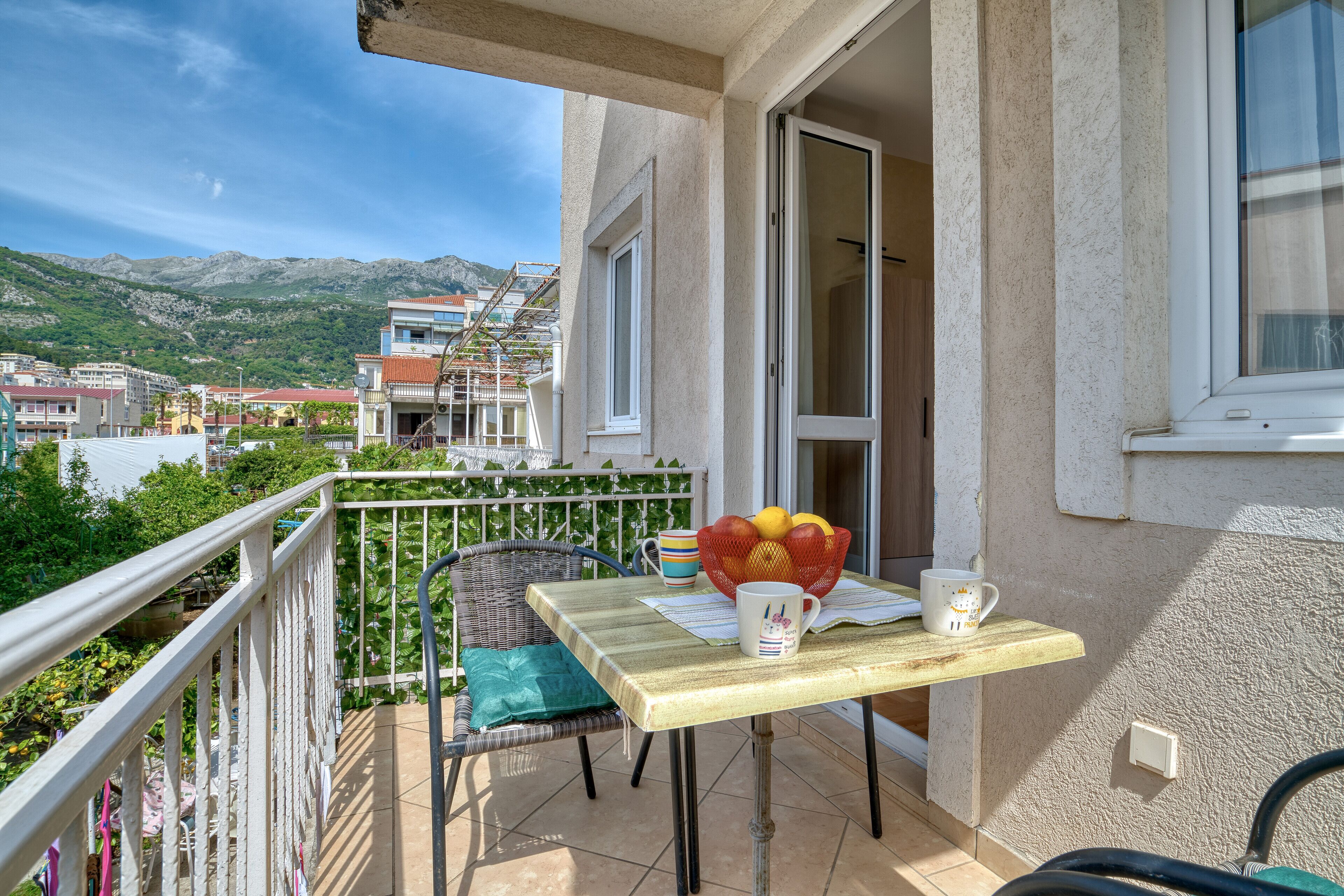 A balcony with a table, chairs, and a view of the town and mountains.