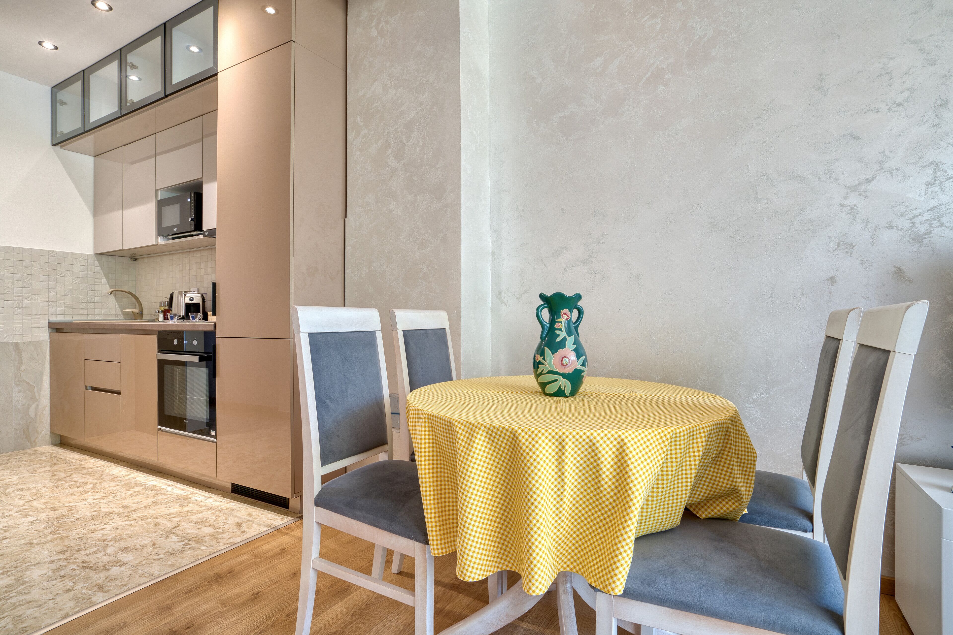 A modern kitchen with built-in appliances, a dining area with a checkered tablecloth, and a vase on the table.