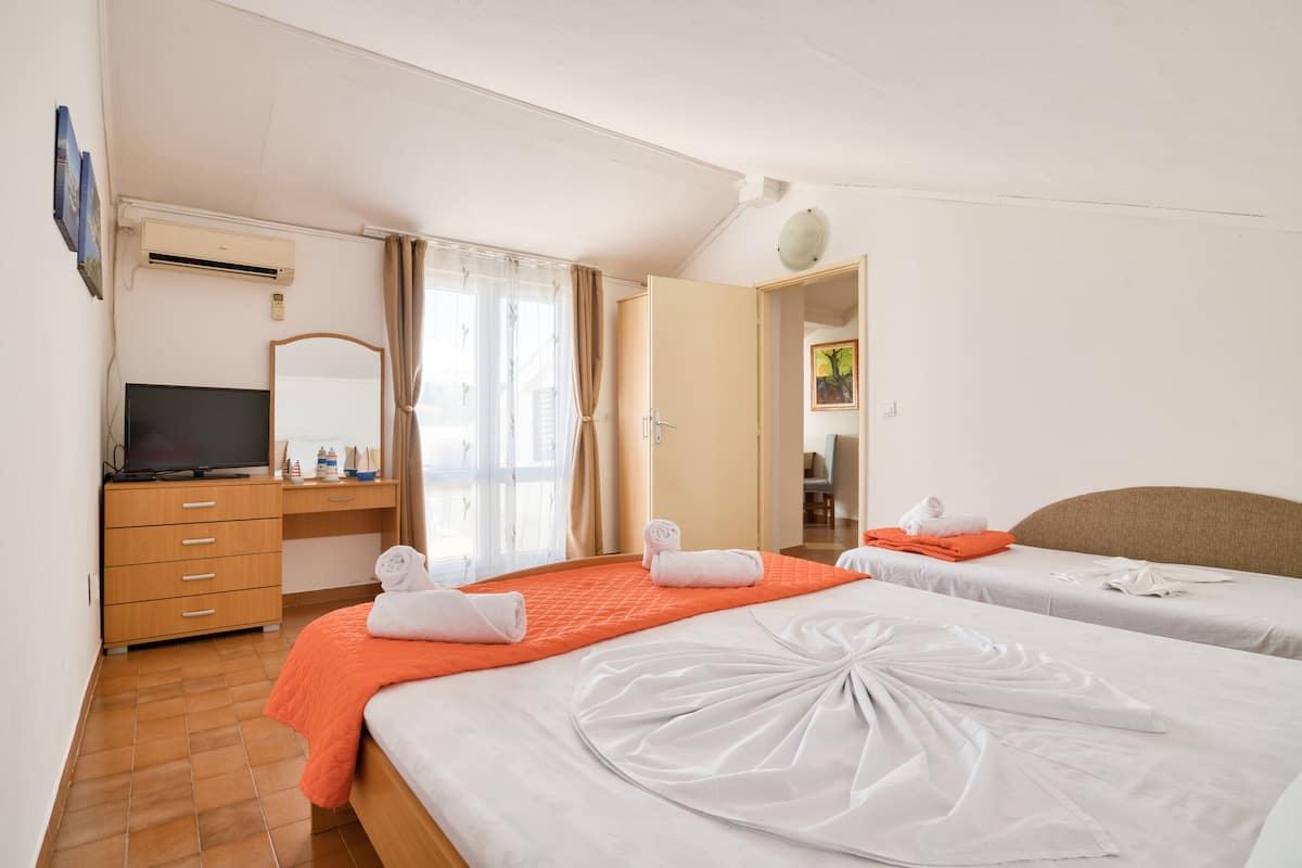 A hotel room with two beds, a desk, a television, and an air conditioning unit.