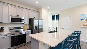 Una cocina moderna con electrodomésticos de acero inoxidable, una isla grande y sillas color turquesa.