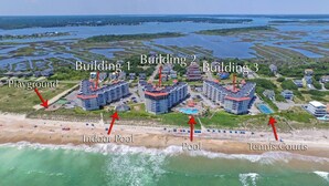 An aerial view of a coastal resort with three buildings, a playground, indoor pool, and tennis courts. - 2 bedroom,  modern oceanfront condo (North Topsail Beach)